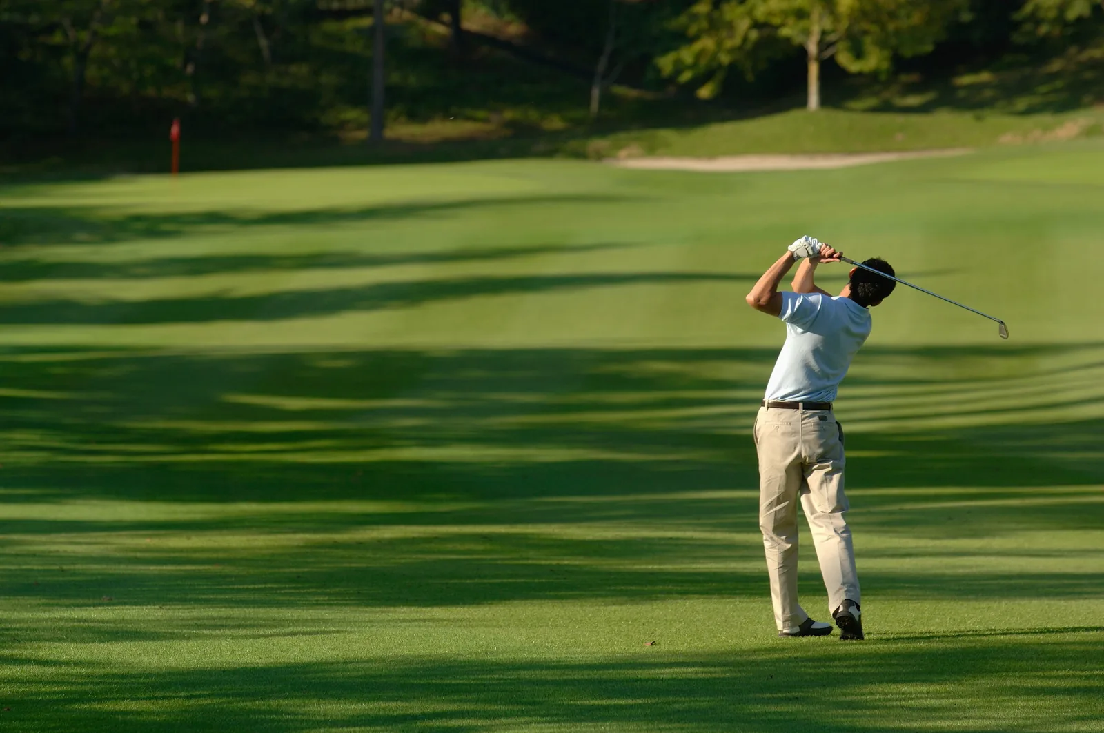 Golfer hitting an iron shot from a rolling fairway